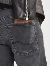 Jean de corte slim fit con tiro bajo, confeccionado en denim elástico de color gris oscuro con efecto lavado. Presenta diseño clásico de cinco bolsillos, cierre frontal con botón y costuras reforzadas.