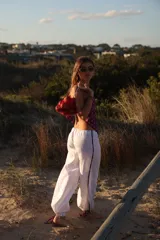 Pantalon de lino color blanco, de corte holgado y estilo babucha, con detalles de franjas estampadas en los laterales y cordones ajustables en los tobillos.