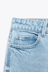 Jeans de mujer, tiro alto, corte Mom Fit con pierna slim y largo tobillero. Denim azul medio con efecto desgastado y lavado. Presenta cinco bolsillos y cierre frontal con cremallera y botón.