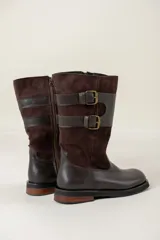 Bota de caña media confeccionada en una combinación de cuero liso y gamuza color chocolate. Presenta un diseño con cierre lateral, doble hebilla decorativa en el lateral externo y suela plana con pequeño tacón.