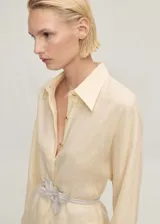 Camisa de lino color crema con cuello camisero, cierre frontal con botones metálicos y mangas largas con puños abotonados.