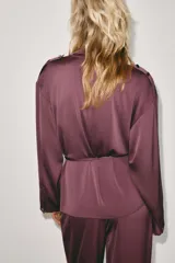 Blazer cruzado de diseño fluido color bordó, con cuello subido, mangas largas, trabillas en los hombros y cinturón fino ajustable en la cintura.