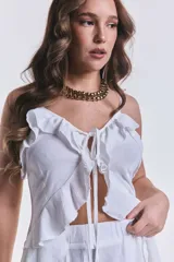 Blusa blanca con breteles finos, detalle de volados en el frente y cordones para atar. Presenta un diseño asimétrico con cola larga en la parte trasera.