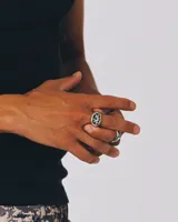 Anillo sello de metal plateado con acabado envejecido y textura rugosa. La parte superior presenta una piedra central de color celeste claro facetada, rodeada por dos estrellas superpuestas con textura. El cuerpo del anillo tiene grabados de estrellas pequeñas.