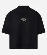 Remera de manga corta, cuello redondo y corte boxy, confeccionada en gamuza sintética (suede) de color negro. Presenta una pequeña estampa localizada en el pecho con un diseño abstracto en tonos dorados/bronce.