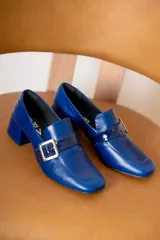 Mocasín de cuero vacuno color azul, con punta cuadrada, taco bloque y tira decorativa con hebilla metálica plateada en el empeine.