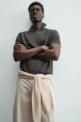 Jersey de punto color verde oliva, de calce relajado (relaxed fit), con cuello solapa y abertura frontal en forma de V. Es de manga corta y presenta acabados en rib en puños y ruedo.