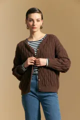 Cardigan de punto color terracota con diseño de trenzas verticales, cuello redondo y cierre frontal con botones metálicos. Presenta mangas largas con puños ajustados y un calce holgado.