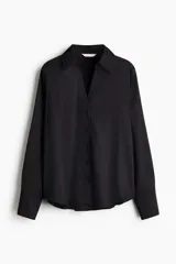 Blusa negra de tela brillante, con cuello clásico, escote en V con botones frontales, mangas largas con puños sencillos y bajo redondeado.