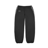 Pantalón deportivo Supreme de color negro, confeccionado en poliéster. Presenta una banda lateral con el logo de la marca repetido y el logo de Supreme bordado en la parte superior delantera. Cuenta con cintura elástica y puños ajustados en los tobillos.