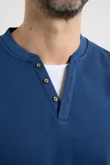 Remera de manga larga en tejido elastizado, color azul, con cuello tipo camisa, cartera con botones y detalles en eco gamuza en la base del cuello y la cartera.