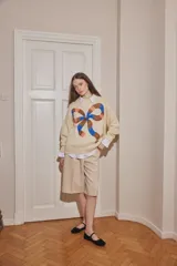 Sweater de lana color crudo, con diseño de moño grande estampado en el frente en tonos marrón, azul y rosado. Presenta cuello redondo, mangas largas con puños acanalados y corte holgado.