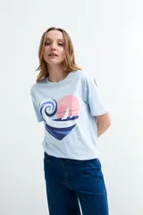 Remera celeste de manga corta y cuello redondo, con estampa frontal en forma de corazón que combina una ola, un atardecer y la frase "Life is Good".