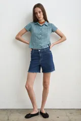 Short de denim azul de tiro medio, corte recto y ruedo con flecos deshilachados.