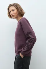 Sweatshirt color ciruela de cuello redondo y manga larga, con detalle de apliques bordados en relieve en las mangas.