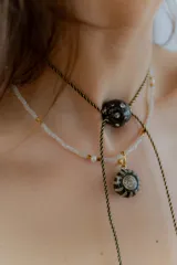 Gargantilla tipo bolo tie de tiento trenzado verde con dije esférico celeste con brillos incrustados.