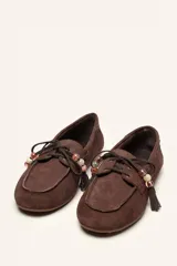 Mocasín estilo náutico de gamuza marrón, con cordones de cuero, borla decorativa y cuentas de colores en el empeine.
