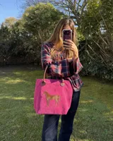Bolso amplio tipo shopper confeccionado en cuero gamuza de color fucsia, con asas de cuero marrón y un aplique de caballo en pelo natural.