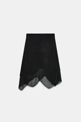 Falda corta negra con efecto metalizado o brillante, cintura elástica y bajo asimétrico con capas superpuestas de tejido ligero.