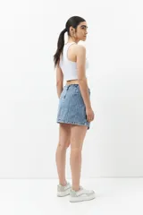 Minifalda de jean celeste con corte asimétrico, bolsillos de parche con solapa y tiras ajustables con hebillas en los laterales.