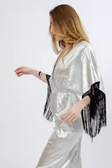 Mono plateado brillante con escote en V cruzado, mangas cortas amplias con flecos negros y cintura elastizada.