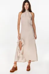 Vestido midi marrón de lino italiano, con cuello halter, sin mangas y diseño asimétrico con volados en el ruedo.