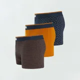 Pack de tres boxers de algodón elástico, uno liso color ocre, uno a rayas horizontales azul y ocre, y uno azul con estampado de hojas color ocre.