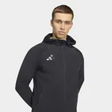 Campera deportiva Adidas del Real Madrid, color negro, con cierre frontal, capucha y corte entallado. Presenta el logo de Adidas y el escudo del club en tono sobre tono en el pecho.