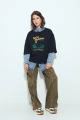 Remera blanca de manga corta con calce relajado y cuello a la base. Presenta un estampado frontal pequeño y una estampa protagonista en la espalda con el texto "Rocky Mountain National Park" y un paisaje de montañas y árboles.