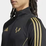 Campera deportiva de entrenamiento negra con cierre frontal y cuello alto. Presenta tres franjas doradas en las mangas y paneles laterales blancos. Lleva el logo de Adidas y el logo de Messi en dorado en el pecho.