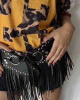 Cinturón de cuero sintético negro con diseño estilo punk, decorado con tachas metálicas plateadas, argollas grandes y flecos largos que cuelgan de la estructura principal.