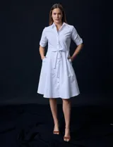 Vestido camisero blanco de algodón con cuello con solapa, delantera abotonada, mangas 3/4 regulables con presilla y botón, y cintura con lazo de ajuste.