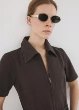 Enterito largo de algodón estilo tejano, color marrón, con cuello camisero, mangas cortas, cierre frontal con cremallera y cinturón ajustable en la cintura.