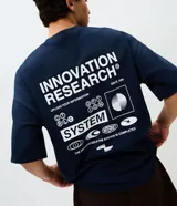 Remera de corte oversized color azul marino, con cuello redondo y mangas cortas. Presenta un estampado gráfico grande en la espalda con el texto 'Innovation Research' y diversos elementos visuales de estilo tecnológico.