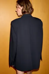 Blazer oversize de corte recto con cuello solapa y cierre frontal cruzado con botones. Presenta mangas largas con hombreras, trabillas en los hombros y grandes bolsillos de plastrón con solapa en el delantero. Incluye abertura en la espalda y forro interior.