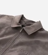 Campera de material sintético en color gris topo, con cuello inglés, cierre frontal por cremallera, mangas largas con puños elásticos y diseño de relieve tribal en la espalda.