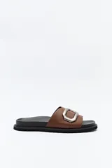 Sandalia slide color beige con hebilla metálica plateada y suela negra.