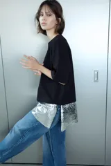 Camiseta negra de corte oversize, cuello redondo y manga corta. Presenta un bajo asimétrico con una aplicación de lentejuelas plateadas a contraste.