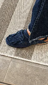 Zueco de cuero color azul marino, con diseño tipo mocasín destalonado, detalles de flecos en el empeine, cordones ajustables y plantilla en tono suela.