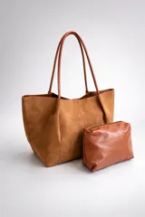 Bolso tipo tote de gran capacidad con acabado efecto gamuza en color marrón tostado, con asas largas para llevar al hombro. Incluye un neceser independiente de cuero sintético liso en tono marrón más claro con cierre superior.
