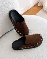 Zuecos de ante color beige con diseño destalonado, punta redonda y tachas metálicas plateadas alrededor de la suela.