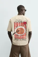 Camiseta relaxed fit color beige, con cuello redondo y manga corta. Presenta un bordado y estampado combinado a contraste en el delantero y la espalda.