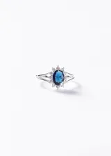 Anillo de plata 925 con piedra central ovalada de zirconia color azul, rodeada por pequeñas zirconias transparentes y banda dividida.