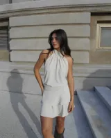 Vestido corto color beige, con cuello halter y espalda descubierta.