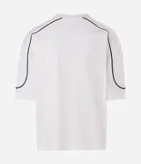 Remera de algodón color blanco, con cuello redondo, manga corta y detalle de raya negra contrastante que recorre la parte superior de los hombros y mangas. Diseño de corte holgado.
