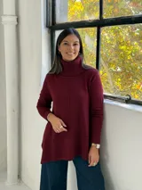 Sweater de punto color bordó con cuello alto tipo polera, diseño de corte evasé con costura central vertical y bajo asimétrico más largo en la parte posterior.