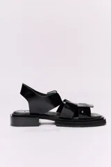 Sandalias negras de cuero charol con plataforma y taco bajo. Presentan tiras anchas con hebilla cuadrada grande en el empeine y tira de sujeción en el talón.