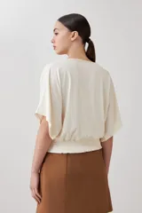 Blusa color beige de tela satinada, con escote barco y mangas cortas.