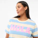Camiseta de manga corta con cuello redondo, diseño a rayas horizontales en tonos azul y crema, y estampa frontal con la palabra 'HOLA' en color rosa.