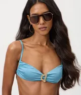 Top de bikini bandeau celeste con acabado satinado, breteles finos y un llamativo aplique metálico dorado en el centro.
